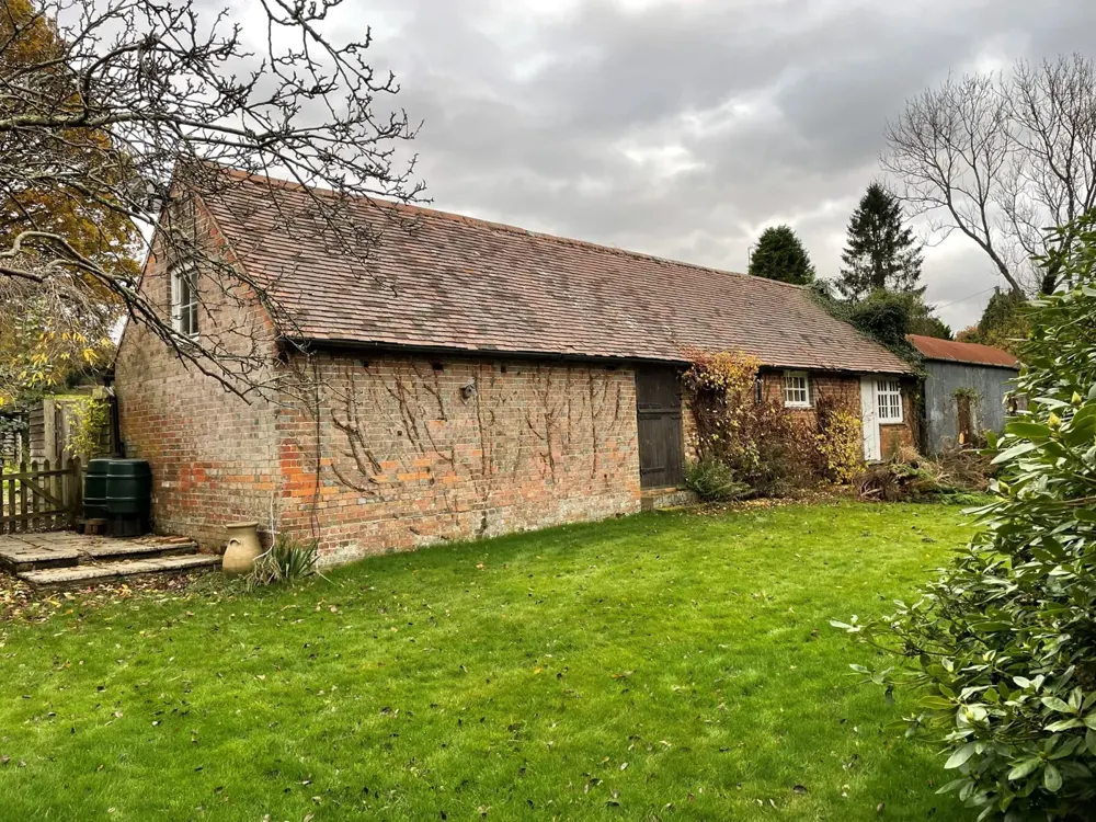 The single-storey brick storage barn at Old Posingford Farmhouse, with a pitched red clay tile roof and climbing plants trained across its garden elevation